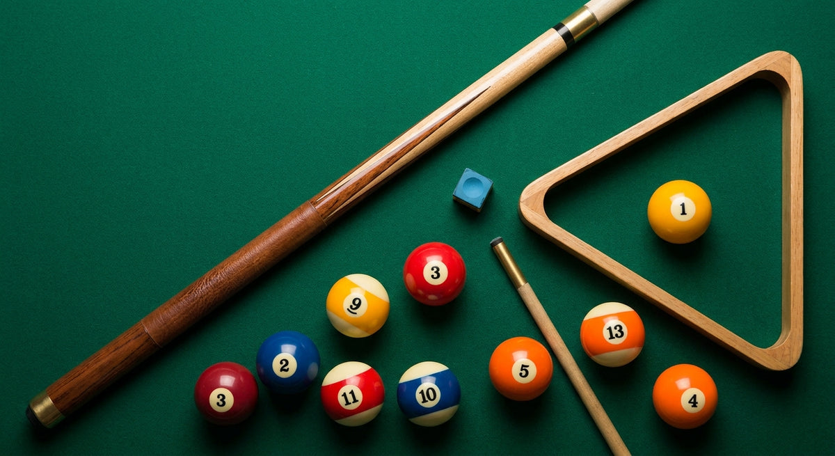 A flat lay of essential beginner billiard accessories including a pool cue, chalk cube, triangle rack, and billiard balls arranged on a green felt surface.